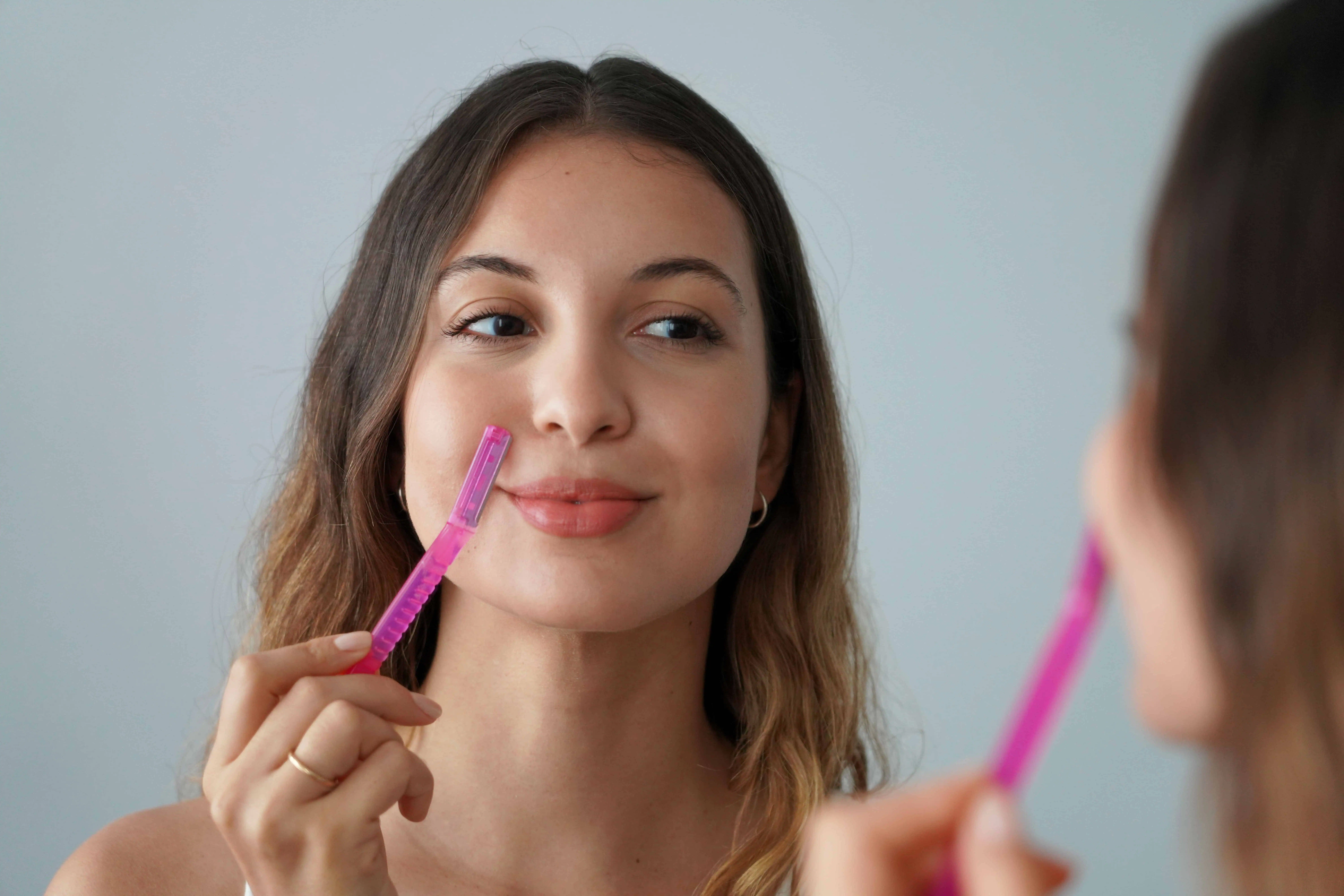 A woman in Bellmore, NY, is dermaplaning her face in a reflection.